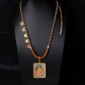 Makroaufnahme einer tibetischen Thangka-Anhänger-Halskette mit buntem Buddha-Symbol - Gelber Jambhala-Blauer Boden