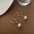 Elegantes pendientes de gancho dorados con perlas blancas sobre superficie de cuero - Gancho de Perla Blanca Curva Geométrica Dorada
