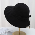 Black wide brim sun hat with ribbon bow on a gold stand against white curtains - Black