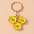 Macro view of golden keychain with three yellow enamel flower pendants on pink background - Yellow