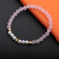 Bracciale di perle rosa opache e perle bianche con ciondolo a stella dorata su tavolo - Quarzo Rosa Stella