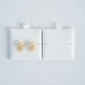 Macro view of floral drop earrings with white pearls and gold base on jewelry display pads - White