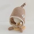 Detail van de gebreide kindermuts met pinguïn-patch en zachte oorkleppen op houten standaard - 54cm (3-8 jaar) / Khaki