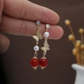 Golden butterfly drop earrings with white pearls and red beads in hand presentation - E3977-1/Gold Butterfly Pearl Red Bead
