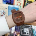 Montre à quartz carrée en silicone marron avec index dorés portée au poignet gauche - café