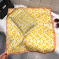 Detailed view of square silk scarf with yellow geometric patterns and pink border on plush rug - Yellow