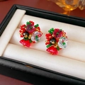 Nahaufnahme handgefertigter Blumenohrringe mit roten und grünen Kristallen auf Satin - Rot-grüne Weihnachtsblume (Silbernadel)