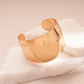 Detailed view of wide gold cuff bracelet on white marble with polished mirror finish - Gold