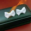Macro shot of white acrylic bow earrings with pearly luster on dark green leather texture - Blue