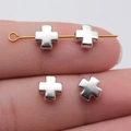 Silver metal cross beads for jewelry making shown on a finger for scale and detail - White Gold