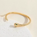 Macro detail of golden snake bracelet with green gem eyes and textured scales on stone - Snake Shape Bangle SL0192-2