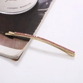 Detailed close-up of a long golden metal hair clip featuring sparkling pink rhinestones - Pink