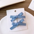 Détail de deux barrettes à nœuds en ruban bleu clair présentées sur une carte blanche - Bleu Brouillard