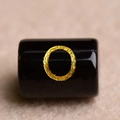 Macro shot of a black cylindrical bead with a textured gold circular pattern for DIY jewelry - Letter O