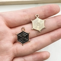 Golden and black spider web alloy charms held in hand for DIY Halloween jewelry making - Black Hexagon Spider Web
