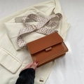 Braune Umhängetasche aus Kunstleder mit gemustertem Schultergurt auf beigem Blazer - Braun