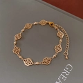 Close-up of a gold clover leaf bracelet with beads and lobster clasp on a dark book - Bracelet - Gold