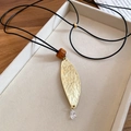 Dettaglio del ciondolo a foglia con perla in resina e cristallo su cordino in pelle nera - Collana - Oro