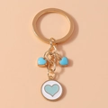 Detalle de llavero dorado con dijes de corazón azul y colgante sobre un fondo color melocotón - Blanco y Azul