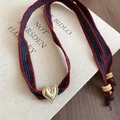 Detailed macro view of woven heart pendant on vintage book with rustic wood textures - Red & Blue Striped Style (Necklace - Red - Blue)