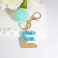 Letter E keychain with turquoise stones, gold foil, and a mint green pompom charm - Letter E