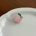 Détail d'une pince à cheveux rose en forme de pêche sur un plateau de décoration blanc - Pêche