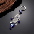 Macro detail of Hamsa hand keychain with blue evil eye beads on reflective black surface - Multi-pendant Silver Hamsa
