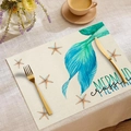 Detail of linen placemat featuring teal mermaid tail print and starfish on rustic table - Mermaid Crossing Starfish