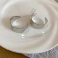 Macro shot of polished silver C-shaped hoop earrings on a textured ceramic plate - Silver