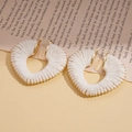 Detail of white yarn-wrapped heart earrings with gold bead trim on a vintage paper background - White