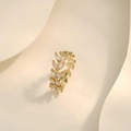 Détail macro d'une bague feuille dorée avec pierres marquises sur fond beige ondulé - Or JZ1073 (Épi de Blé Feuille Zirconium)