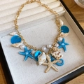 Close-up of gold necklace with blue starfish and shell charms in a jewelry box - Gold Blue White