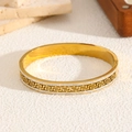 Détail du bracelet doré ajouré avec motif grec et bordure ornée de cristaux scintillants - Doré