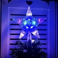 Nahaufnahme der transparenten Stern-Baumspitze mit blauer LED auf einem grünen Zweig - 15cm Gestreift Mehrfarbig (2x AA Batteriekasten)