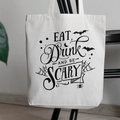 White canvas tote bag with Eat Drink and Be Scary Halloween print hanging on a black chair - 35cmx40cm
