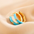 Macro detail of sky blue enamel gold hoop earring with a central clear zircon inlay - Blue