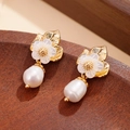 Golden flower earrings with natural baroque pearl drops on a warm wooden surface - White