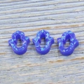 Close-up of three blue glitter resin Hamsa hand charms on a blue wood background - Blue