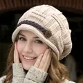 Close-up of beige knit beanie with woven leather strap and vintage metal button detail - Beige