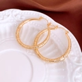 Makroaufnahme von goldenen Creolen mit Diamant-Hammerschlag-Textur auf einer Keramikschale - Mittel / Gold