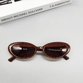 Occhiali da sole ovali vintage marrone scuro distesi con uno sfondo di libro decorativo - caffè