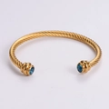 Goldenes Kabel-Armband mit blauen Edelsteinen an den Enden vor neutralem Hintergrund - Gold mit blauem Zirkon