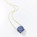 Detail shot of a natural raw blue crystal pendant on a thin gold chain against white background - Blue Sodalite