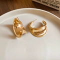 Gros plan détaillé des boucles d'oreilles dorées en forme de C sur une assiette blanche - Doré
