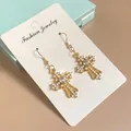 Golden cross drop earrings with pavé zircons and oval center stone on a display card - Earring Hooks / Gold White Zirconia