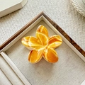 Glossy orange gradient frangipani hair claw clip placed on a beige jewelry display tray - Bright Orange