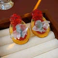 Makroaufnahme von irisierenden Goldfisch-Ohrringen mit roter Rose auf Bernstein-Basis - Rote Blume Transparenter Fisch Bernstein Basis