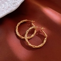 Dettaglio di orecchini a cerchio dorati con texture martellata su seta rossa di lusso - Cerchi Oro / Oro