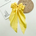 Detailed view of yellow satin bow hair clip with elegant long ribbon tails on a white book - Yellow