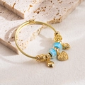 Détail d'un bracelet doré à perles en verre bleues et breloques en forme de cœur sur pierre - Bleu